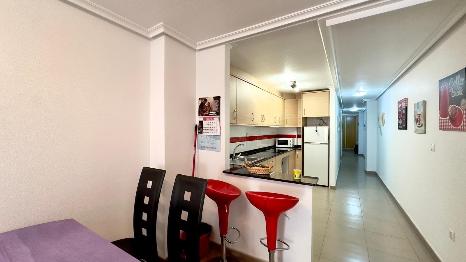 Cozy and functional 2-bedroom, 1-bathroom apartment on one of Torrevieja's most central and sought-after streets, the well-known Calle Apolo, a pleasant walk from the beach and surrounded by all amenities year-round. Surroundings and Location Living on Calle Apolo means enjoying the authentic heart of Torrevieja, in a well-established urban area, well-connected and with a wide range of shops, supermarkets, banks, cafes, and restaurants just steps from your door. The main shopping streets, such as those near the seafront promenade and Plaza de la Constitución, are just a few minutes' walk away, allowing you to run your daily errands without needing a car. Playa del Cura and the marina are also a short stroll away, making this apartment an ideal option for those who want to combine urban living with proximity to the sea on the Costa Blanca. Building and Residential Atmosphere The apartment is located in a contemporary building typical of Torrevieja's city center, with a well-maintained entrance and a primarily residential atmosphere, where families and young couples live side by side. and foreign residents who have chosen the city for its climate and quality of life. Apolo Street is made up of multi-story apartment blocks, with shops on the ground floor and apartments above, creating a lively environment during the day but a peaceful one at night, perfect for permanent living or as a second home. It is a flat, walkable area with paved streets and an orderly urban layout, facilitating access for people of all ages and making daily commutes comfortable and pleasant walks. Interior Layout Upon entering the apartment, a foyer leads to the living area, where the living-dining room is arranged around the open-plan kitchen, creating a single spacious and practical area that makes the most of the available space. The layout naturally separates the social area of ​​the apartment from the sleeping area, where the two bedrooms and bathroom are located, providing privacy for families or those who wish to combine living and working remotely. The interior design follows the concept of a functional urban apartment, with narrow hallways and well-proportioned rooms. Proportioned, designed to offer comfort in daily use without sacrificing distinct areas for relaxing and entertaining. Living-dining room The living-dining room is the heart of the home, a bright space that receives natural light from the balcony and is ideal for both relaxing and gatherings with friends and family. Its rectangular layout allows for a comfortable sofa facing the television area, as well as a dining table for several people, creating a versatile environment that adapts to different decorating styles, from the most modern to the most Mediterranean. The direct visual connection with the open-plan kitchen and access to the balcony reinforce the feeling of spaciousness, making this a fluid space where daily life unfolds naturally, from leisurely breakfasts to more social evenings. Equipped open-plan kitchen The home features an equipped open-plan kitchen that integrates seamlessly into the living area, offering a comfortable and modern solution for those who value practicality and direct contact with the rest of the house while cooking. This type of kitchen facilitates communication with the living room and allows for easy access to the dining area. Guests or family members can enjoy meals while cooking, and the design allows natural light from the balcony to reach the work area. The furniture and countertop layout is designed to maximize space, with an organized cooking, preparation, and storage area, ideal for both vacation use and year-round living in the apartment.