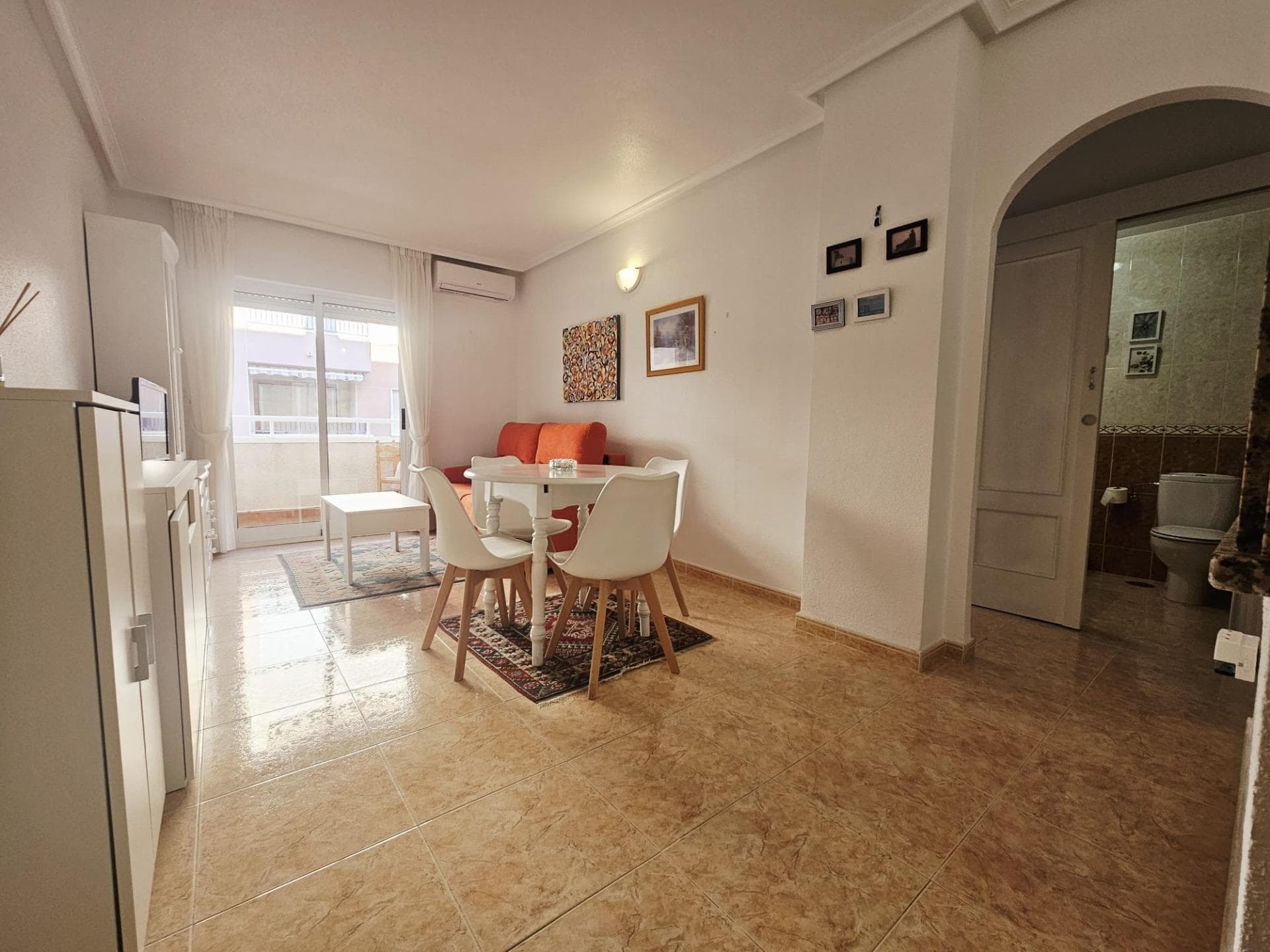 At 1 San Luis Street, the surroundings invite you to imagine a comfortable and relaxed lifestyle, right in the heart of Torrevieja and very well connected to essential daily services. Just a few minutes' walk away are shops, leisure areas, and points of interest, making this location a very practical option for both year-round living and enjoying holiday stays. Surroundings and Lifestyle The street is located in a well-established area with an orderly urban layout where residential buildings, small businesses, supermarkets, and local services coexist, making daily life easier without needing a car. The presence of nearby bus stops allows for convenient travel throughout the city, connections to the bus station, and access to other towns on the Costa Blanca. The neighborhood's atmosphere combines the tranquility of a residential area with the characteristic vibrancy of Torrevieja's city center, offering a dynamic environment without sacrificing peace and quiet. In addition, the area offers pharmacies, schools, clinics, and small specialty shops that cater to the daily needs of any resident year-round. Connection to the city and the sea From this location, you can reach the heart of Torrevieja in just a few minutes, with its shopping streets, cafes, restaurants, and seaside promenades. This proximity to the city center makes it easy to enjoy cultural and festive activities, as well as local markets, nightlife, and administrative services without long journeys. The coast and seafront promenades are within easy reach, making it simple to incorporate the sea into your daily routine, whether for a stroll, sports, or simply relaxing by the Mediterranean. The city of Torrevieja is known for its mild climate and long periods of sunshine, so outdoor activities can be enjoyed practically all year round. Building and Common Areas The property is part of a multi-story residential building constructed in the early 2000s, with standard quality construction that reflects the functional and practical style typical of the area. The building has an elevator and an entrance designed to facilitate access for residents of all ages, as well as well-designed interior circulation areas.  On the rooftop or within the complex, there is a communal swimming pool that becomes a true meeting point during the warmer months. This space for swimming and relaxation allows residents to enjoy the Mediterranean climate without leaving the building, creating a relaxed and pleasant atmosphere among neighbors.  Impressions Upon Entering the Apartment Upon crossing the threshold, you will find a welcoming atmosphere, designed to make the most of every available square meter and create a clear separation between the living area and the sleeping area. The layout promotes continuity between spaces, making the transition from the entrance to the main area feel natural and fluid. Natural light plays a starring role, filtering through the openings onto the terrace and creating different nuances throughout the day. This luminosity contributes to a warm atmosphere in winter and is especially pleasant on sunny days, reinforcing the feeling of home from the moment you step inside.  Daytime Living Area The heart of the home is a spacious area dedicated to daily activities: moments of relaxation, gatherings with friends, family meals, or leisure time in front of the television. The visual integration with the kitchen area creates a dynamic and social atmosphere, ideal for those who enjoy conversation while preparing meals or sharing a coffee.
