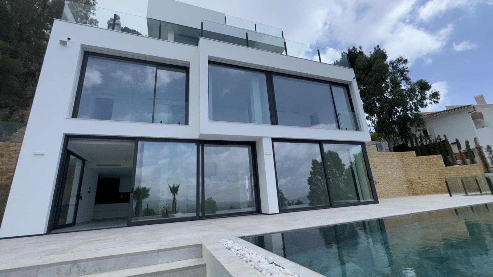 A modern villa with panoramic views of the sea and mountains, located in the secure and prestigious urbanisation "Altea Hills", renowned for its breathtaking views, impressive villas, and guaranteed peace and privacy. Upon entering the plot, you’ll find an open parking area for 2 cars, as well as a spacious open space with stunning views of the sea and mountains. Going down the stairs, you arrive at the upper level of the villa, next to the main entrance and the lift. To the left of the main entrance, there is a cloakroom for coats. On the next floor, there are 4 bedrooms, each with its own en-suite bathroom. Every bedroom has space for a built-in wardrobe, while the master bedroom features an additional room that can be used as a separate dressing room or a child’s bedroom. The main bathroom includes both a shower and a jacuzzi. The lowest floor houses a spacious living room with an open-plan kitchen and dining area. Next to the kitchen is a utility room, ideal for a washing machine, freezer, and other household appliances. This level also includes a guest bedroom and a guest toilet with a shower. From the living room, you step out onto a large terrace with panoramic sea and mountain views, an infinity-style pool, and a barbecue area. An outdoor shower is installed next to the pool. The house is equipped with air conditioning, underfloor heating, and a smart home system.