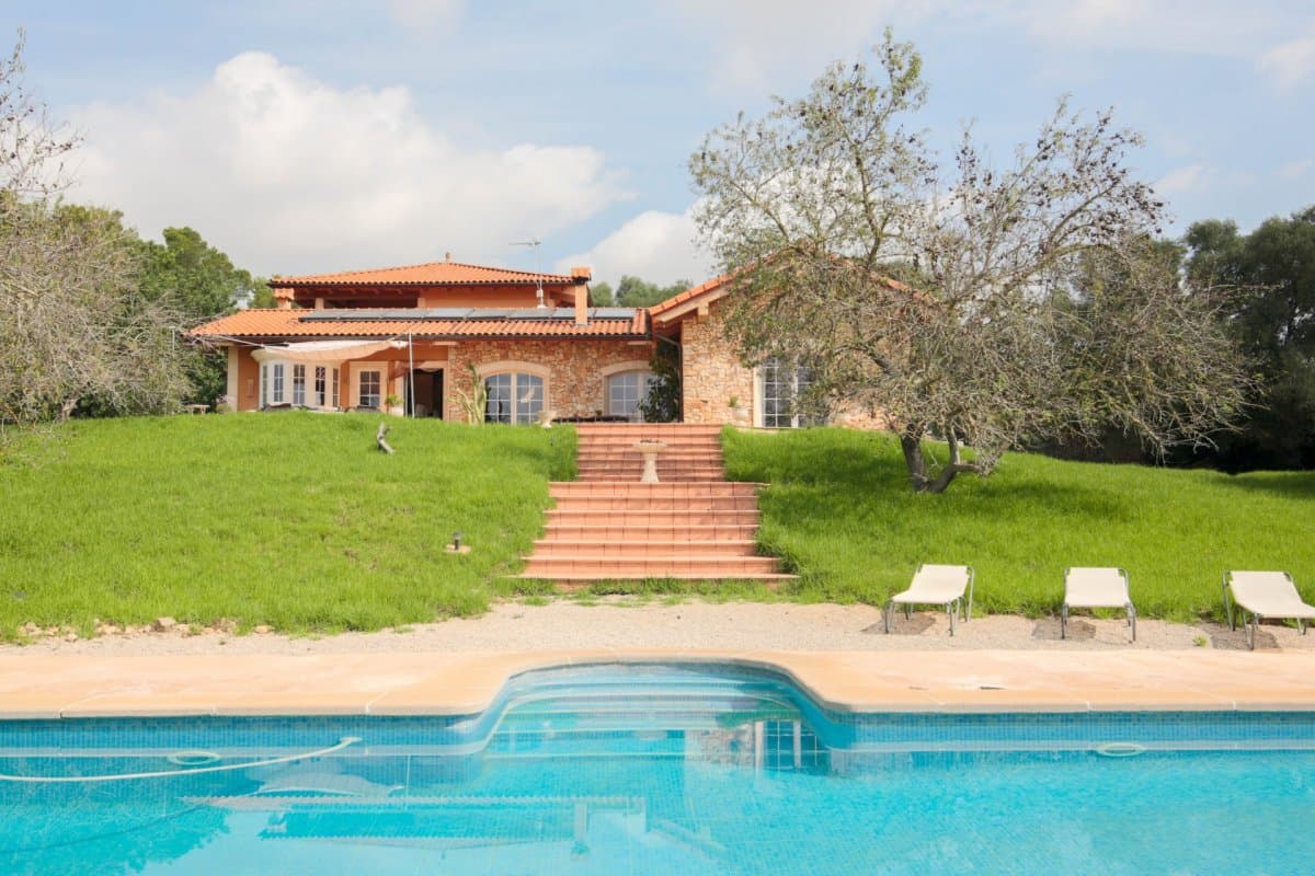 We present a charming house located on an extensive rustic property in Montuiri, surrounded by the serenity and natural beauty of the typical almond and carob trees of the island. This property is distinguished by its tranquility, with almost no close neighbors, and offers a perfect refuge for those seeking privacy and contact with nature.. . The ground floor is distributed in a large entrance hall with a semicircular staircase with a stainless steel railing, which connects the three floors, a large living room with a biomass fireplace and direct access to a large terrace, a large open kitchen with a pantry, a large dining room with direct access to another terrace, two double bedrooms with built-in wardrobes and two complete bathrooms with walk-in showers and bathtubs, one of them en suite. One of the bedrooms has direct access to one of the terraces.. . The upper floor is distributed in an open area used as an office, a double bedroom with a built-in wardrobe and a large bathroom with shower and bathtub and a covered terrace. On the semi-basement floor, it is distributed in a double bedroom with a built-in wardrobe, a storage room with the facilities prepared to convert into a toilet, a large garage with space for 1 vehicle, a laundry room and a machine room for heating.. . Outside the house there is a large swimming pool surrounded by terraces with a covered summer kitchen with toilets and storage room, there are also several sheds used as storage rooms and an artificial pond. The house is equipped with PVC double-glazed security windows, alarm, air conditioning and underfloor heat pump, heating with biomass fireplace, water softener, vacation rental license and is sold fully furnished and ready to move into. to live.. . The property has a water well, but the electricity is through a solar panel system.. . This property in Montuiri is a unique opportunity to acquire a house that combines modern comfort with rustic charm, offering a relaxed and sustainable lifestyle. Perfect both as a permanent residence and as a vacation rental investment, this estate is ready to welcome its new owners and offer them an oasis of peace and natural beauty.