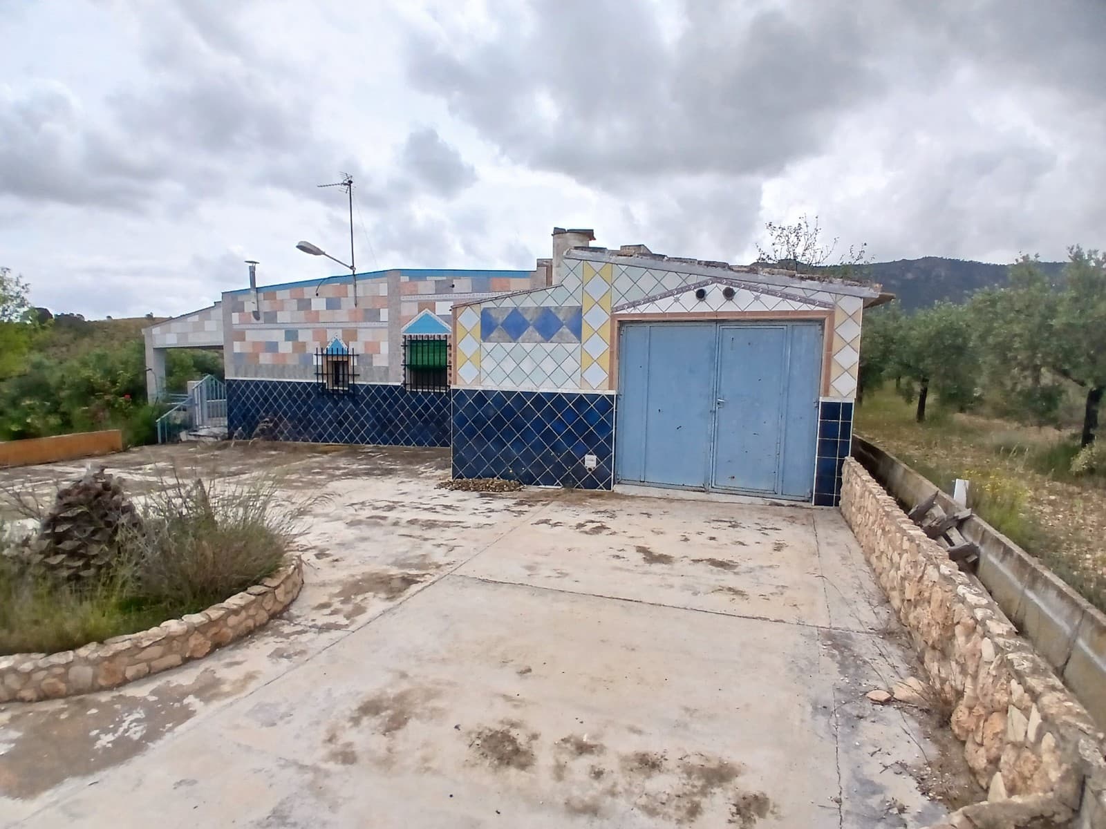 If you love peace and quiet and nature this is the place for you. The property has a good size living room with fireplace, a kitchen of 6.07m2 and 5 bedrooms of 7.46m2, 10.92m2, 9.31m2, 8.88m2 and 9.12m2, there is also a small bathroom of 3.47m2, with toilet, sink and bidet. Outside you will find another bathroom with shower of 4m2.Outside is a porch of 12.62m2 where you can enjoy the views of the garden and the mountains. There is also a pool of 19.25m2 and there are 2 garages, 1 next to the house of 22.76m2 and one behind the property of 12.09m2. Furthermore there is a barbeque area of 10.85m2.The windows all have single glass, mosquito nets and wooden shutters.The structure of the house is in good condition, there are no moist problems. However the whole house needs to be repainted and the bathroom and kitchen need updating. The house has no electricity, it has been used as a holiday home and they have one old solar panel for light, the kitchen is all on gas, including the fridge. A new solar installation is required (off grid solar system set from Obramat costs 7.000 euro incl back up generator). They have mains irrigation water and 2 water deposits, one to collect the rain water and another they used previously to be fill with drinking water by truck. The large plot of almost 4.000m2 has several olive trees, as well as almonds, figs, mispel and grapes.This remote country property is located on 9km from Yecla and has a 2 km long non-asphalted access road. Even though it is remote there is still 4G reception and there are a few neighbors around.