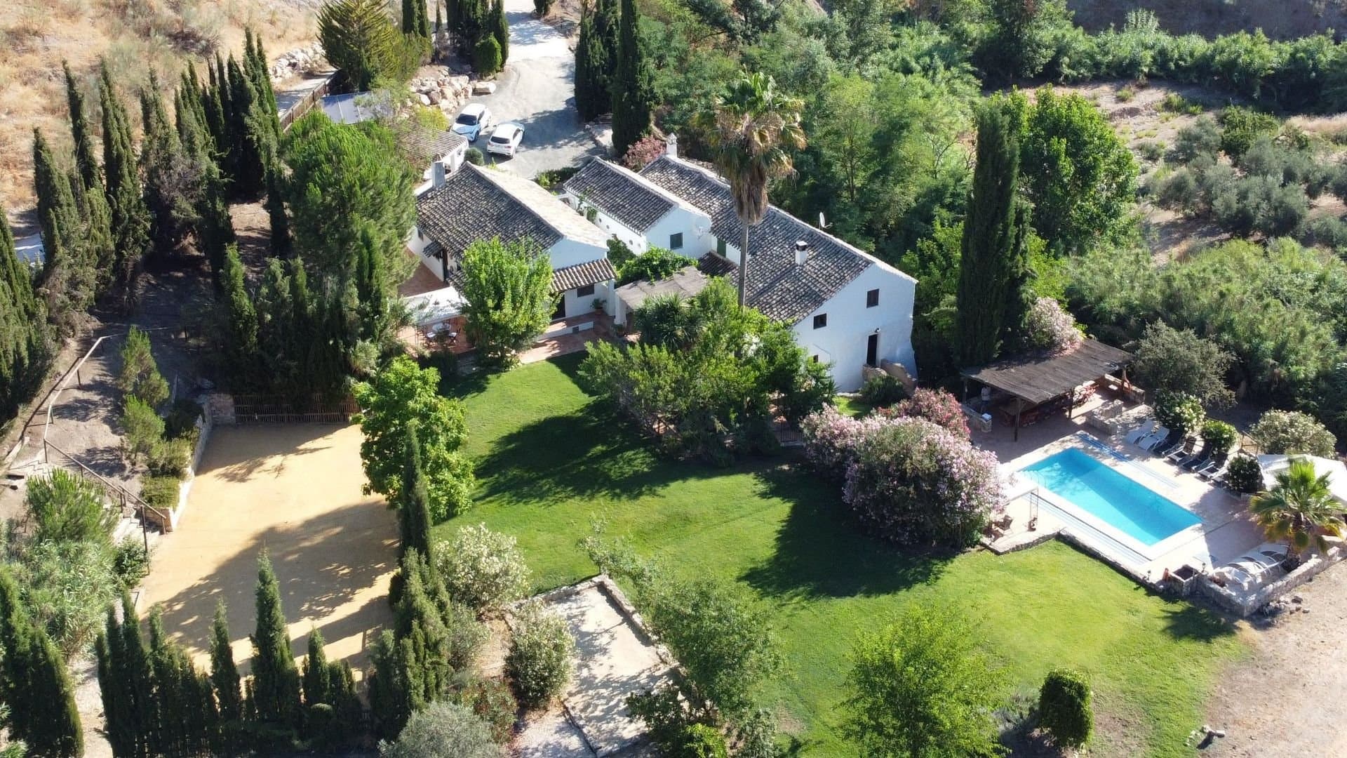 A beautiful large white Andalucian mill house, currently used for holiday rentals, with 10 bedrooms, 7 bathrooms, and private swimming pool, set in large, secluded gardens. It is a fantastic property that has everything to offer and more! The house is surrounded by hills and olive groves near the lovely Lake Iznájar and with excellent access to the vibrant cities of southern Spain: Granada, Seville, Córdoba, Ronda and Málaga. This unique and beautiful Andalucian Cortijo was a working water mill and bakery until the end of the 20th century, supplying bread to local farms and villages. The Old Bakery kitchen still features the original bread oven, but now has a restaurant grade cooker and a dishwasher too. In the grounds, you will find fresh herbs from the kitchen garden, pomegranate, fig, peach, and almond trees, sunny terraces, and a floodlit sports court, ideal for tennis, volleyball, or badminton. There is also a studio for indoor cinema (with projector and screen), yoga and Pilates and there is a Petanque Pista (the Spanish version of Boules), ping pong table, sandpit and of course a lovely private swimming pool. The exterior also boasts shaded dining areas, picnic spots next to the stream, a vine-covered courtyard, and big private gardens where children can run around safely. The land is flat and would be ideal for horses. Lovingly restored to retain all the character of the big old mill house, the accommodation is arranged into two wings around a central courtyard. The eastern wing of the house is renovated from the old mill, retaining its original features, with the main kitchen, living and dining rooms together with 5/6 bedrooms and 4 bathrooms. The other wing was formerly the house of the master baker and has 4 bedrooms, 3 bathrooms and a second kitchen. This stunning property offers the option of having breakfast on the kitchen terrace (watching the antics of the ducks and listening to the hens laying your morning eggs), lunch in the vine-shaded courtyard, or ramble down to the stream with the children for a picnic tea and enjoy dinner by the pool in the evening. If you prefer to entertain guests indoors the dining room can seat up to 18 people and you can easily spread out into the adjacent Old Bakery kitchen which seats a further 10 guests.