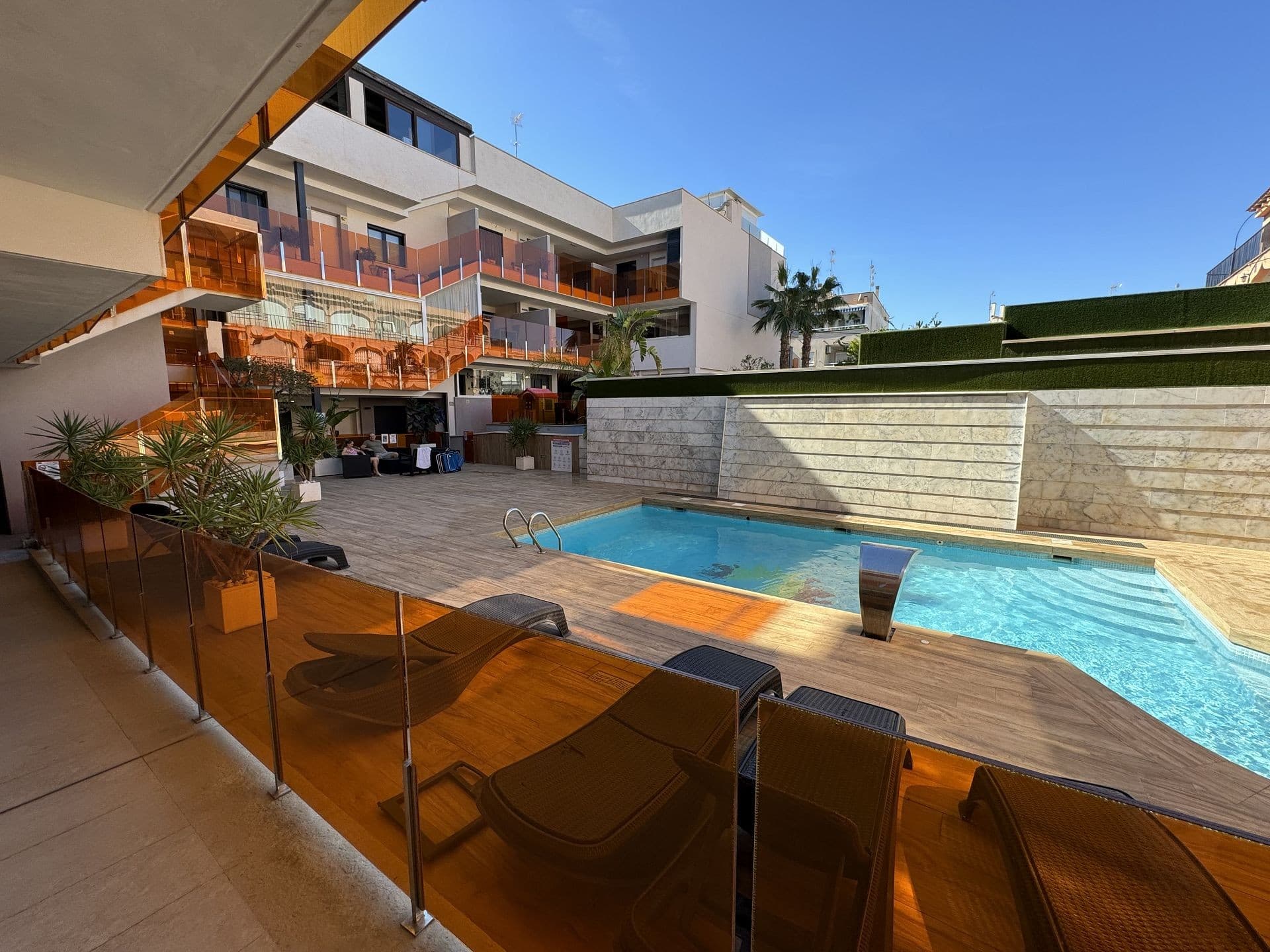 APARTMENT IN TORREVIEJA. Come visit a beautiful two-bedroom ground-floor apartment in the “Alegria 1” residence in Torrevieja, Spain. It is conveniently located just five minutes from the beaches of the Mediterranean, in the city centre and close to all amenities. The building has an underground parking space as well as a rich infrastructure. The ground floor has a comfortable recreation area with a large swimming pool, sauna and playground. You can also enjoy the sun on the communal roof terrace. It has an open kitchen with a living area, fitted wardrobes and a swimming pool open all year round. The common areas include a communal solarium with a BBQ, a relaxation area and a children's playground. The building is just 700 meters from the city beach and close to all services (supermarkets, town hall, bus station, health centre). Golf courses are only a few kilometres away, and sandy beaches with natural pine forests are only 2 km away. Torrevieja is a quiet city; all services, such as restaurants, bars, shops, banks, leisure areas, etc., are available all year round. Every Friday, a market is organised in the city, and many people buy local products. Torrevieja has a large marina with activities all year round, a large sports centre with paddle tennis, tennis, and football, and a large heated swimming pool open all year round. There is also a library with free Wi-Fi and computers. Torrevieja is only 45 km from Alicante-Elche Airport (El Altet), from where, due to the demand for tourists on the Costa Blanca, many flights depart daily with connections to the main European cities. 