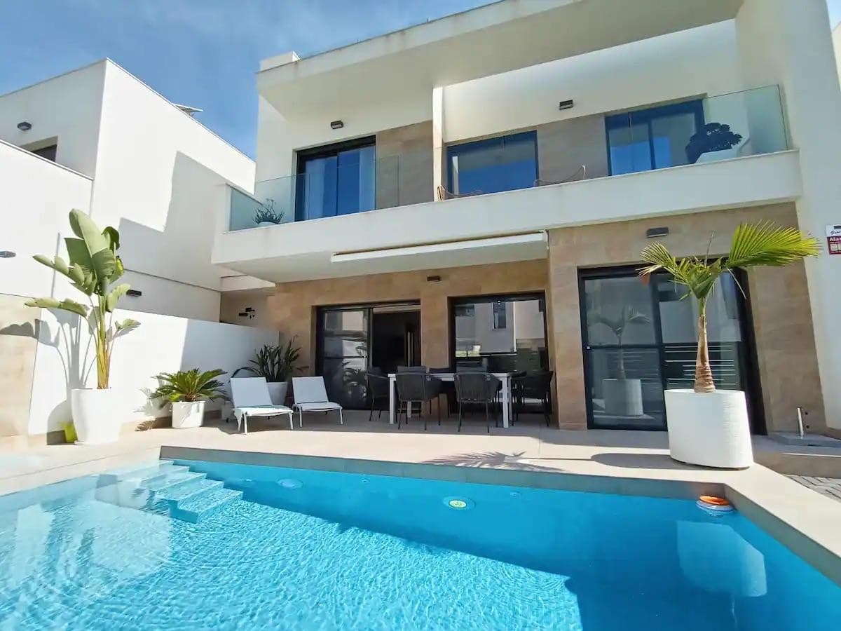 This modern villa, constructed in 2021, epitomizes contemporary design and luxury living. Situated in La Herrada, Los Montesinos, the villa covers a build size of approximately 115m² on a south and east-facing plot of 225m², ensuring ample natural light throughout the day. The ground floor is a testament to open-plan living, featuring a spacious kitchen seamlessly integrated with a lounge and dining area. Three expansive picture windows flood the space with light and provide unobstructed views of the private pool and a large sun terrace, perfect for outdoor relaxation and entertainment. The villa boasts three generously sized bedrooms, each fitted with ample closet space. Two of these bedrooms include en-suite bathrooms, offering privacy and convenience. One bedroom stands out with its access to a large balcony, an ideal spot for morning coffee or evening relaxation. In addition to the terrace and balcony, the villa includes a large solarium, providing breath taking views of the surrounding area, including the stunning salt lakes. This property is an excellent choice for those seeking a modern, stylish home in a peaceful yet well-connected area.