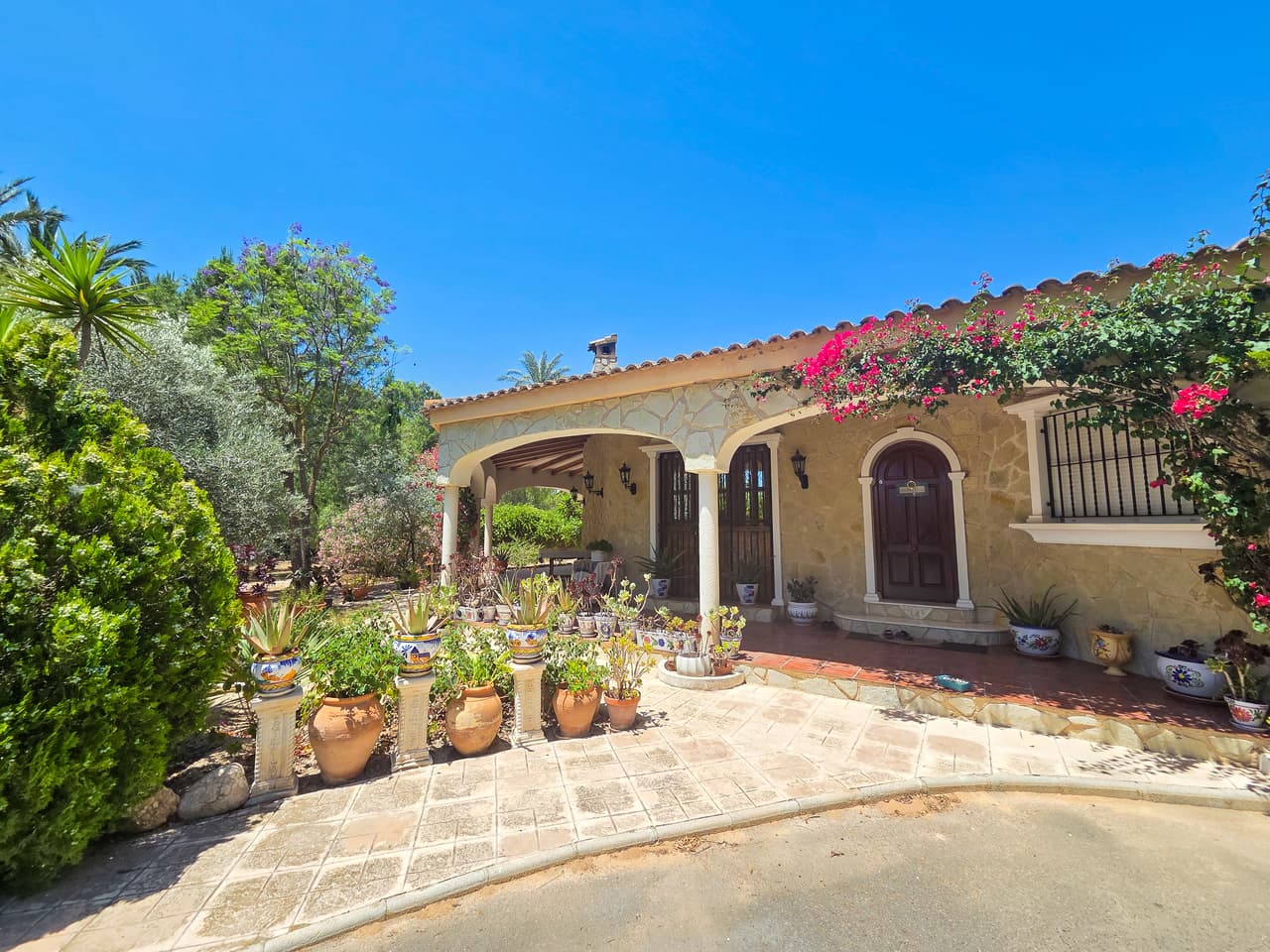 This unique single-level country estate stands out for its striking, rounded architecture, distinct character, and incredible potential. Stepping through the entryway to the left, the heart of the main home features a spacious lounge with incredible architectural details such as wooden beams, arched windows looking out to the interior yard, and a feature stone wall. To the right of the entryway is a fully equipped independent kitchen complete with traditional features and beautiful granite countertops. Custom stained-glass windows highlight the home's unique architectural lines. The layout wraps elegantly around a central internal courtyard featuring a fountain and direct stairs leading up to the rooftop solarium. The main villa cleanly distributes four large bedrooms and a private study across the floor plan, alongside two bathrooms, all connecting smoothly to expansive covered porches. There is also a large garage currently converted into extra living space.Set on an expansive plot designed to enjoy the Mediterranean climate, the outdoor space features two large porches, a 53 m² private swimming pool, and gardens filled with mature palm, pine, and fruit trees. The exterior of the property does require some general maintenance and retouch work—it needs a bit of love, but the structural character and upside potential are massive. Excellent guest and wellness features are already built, including a completely detached guest wing with one independent bedroom and bathroom, two independent ground-floor flats with a living area, kitchen, and bedroom with en-suite, a registered wooden Finnish sauna, and a private covered Jacuzzi cabin.Practicality meets versatility with a separate 85 m² social lounge located right next to the pool terrace, making it an ideal space for large family gatherings, a fitness/yoga studio, or a commercial event room. Furthermore, the adjacent plot comes with a second house to reform.The location offers total privacy right next to the peaceful nature reserve, while keeping everyday conveniences within easy reach. You are just a 15-minute drive from Elche’s historic city center and 15 minutes from the beach. Travel is straightforward, with quick access to Alicante airport.