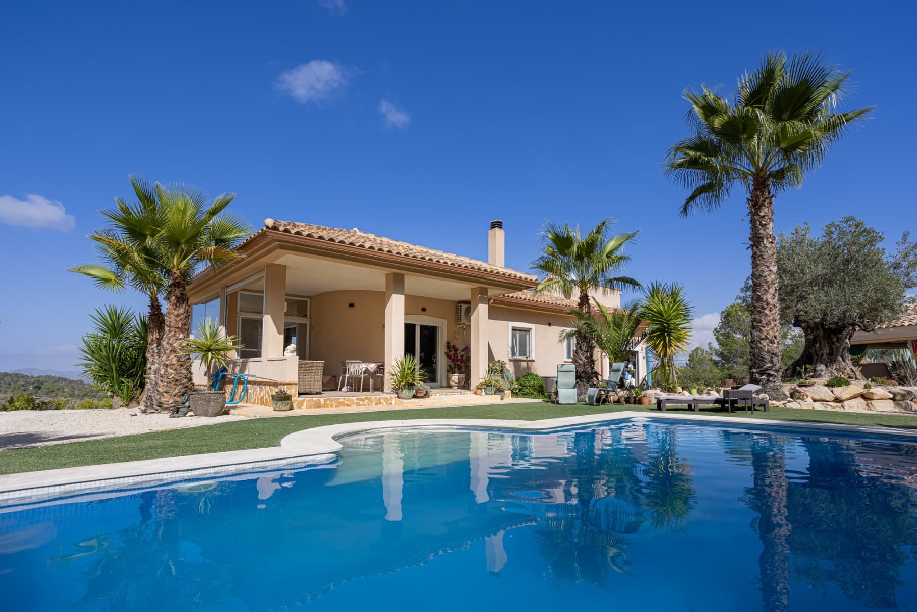 We present this beautiful detached villa, situated in a unique natural setting in La Zarza, where the tranquility of the countryside is combined with all modern amenities. Ideal as a permanent residence, holiday home, or even as a rural investment. Layout and interior spaces With a built area of 144 m², this charming home offers a functional and bright layout. The house features three spacious bedrooms (one of which has been converted into a garage, but is easily convertible), all with abundant natural light, and two carefully finished bathrooms, as well as a guest toilet for added convenience. The open-plan kitchen, fully equipped with appliances, flows seamlessly into the living-dining room, creating an open and welcoming space, ideal for enjoying with family or friends. The living room features a cozy wood-burning stove, perfect for winter evenings. The house also has central heating (propane) and air conditioning for optimal comfort year-round. One of the most special features of this property is the underfloor heating throughout and the use of a unique water system connected to the gas central heating system. The house is fully furnished and equipped, move-in ready, and features built-in wardrobes for extra storage. The master bedroom boasts a fantastic walk-in closet and an en-suite bathroom. A real eye-catcher in this bathroom is the jacuzzi with shower. The walk-in closet can even be converted into an additional small bedroom if desired. The house has 18 electric solar panels (On-Grid) for the house and another 6 panels for the solar boiler (house hot water, swimming pool heating). Exterior: Nature, privacy and outdoor recreation The true luxury of this property lies outdoors. Situated on an impressive 13,400 m² plot, surrounded by nature, it offers complete privacy and spectacular open views of the landscape. The meticulously maintained garden leads to a fantastic private swimming pool, ideal for cooling off in the summer, but also heated for cooler winter days. It also features a barbecue area, a covered veranda perfect for al fresco dining, a large sun terrace, and a solarium for enjoying unforgettable sunsets. There is also a closed garage and a private parking space on the plot. Location and accessibility Although the villa offers complete tranquility, it is very easily accessible: Recreation areas, restaurants and amenities are just a 10-minute drive away. Prestigious golf courses are 40 minutes away. Both the Mediterranean beaches and the nearest airports are within 60 minutes, making it an excellent choice for regular day trips or international visits. The south-west facing location guarantees sunshine and spectacular natural light for most of the day. Included extras Air conditioning Electric roller shutters (persianas) throughout the house Central heating (propane gas, 1000 liter tank) Water tank (21,000 liters) Fireplace (for wood) Solar panels (as support, the house is also connected to the electricity grid) Furnished Appliances (main kitchen appliances) Barbecue and outdoor seating area All automatic gates are operated with GSM WiFi Private swimming pool (heated by solar boiler) Garage and parking space Veranda, terrace and solarium Large private garden