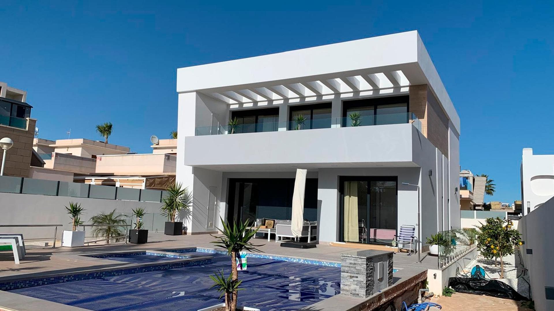 For sale is a large 4-bedroom, 4-bathroom villa with a natural fireplace, built in 2026, on a flat, straight 500m² plot with a private heated pool and parking for 2 cars opposite the park behind the Budapest restaurant in Quesada-Rojales. This quiet, beautiful location is opposite a subtropical park with ficus trees and views of the Pink Lagoon of Torrevieja, behind the Budapest restaurant in Quesada-Rojales. Nearby are a language school, numerous shops and restaurants, and a Consum supermarket. The villa is spacious – the total area is 341m², the living area is 213m². The house is built on two floors with a steel staircase between floors. The third level is a huge solarium overlooking the Pink Lagoon. The house consists of the following on the first level: - 9 m² entrance hall, - 37 m² living room with access to a 19 m² covered terrace, - 27 m² open kitchen "Island" with all Bosch appliances and a toilet, - 13 m² first bedroom with a walk-in closet and bathroom, The second level of the house includes: a 9 m² hallway with access to an 18 m² balcony, three separate bedrooms: 15 m² and 14 m², each with a built-in closet and a 7 m² balcony, a 22 m² master bedroom with several built-in wooden wardrobes and a large bathroom with a Jacuzzi. A steel staircase with wooden steps leads to the third level of the house – a 109 m² solarium. The house is equipped with: - a natural fireplace - central air conditioning with a "hot/cold" function - a heated underfloor water pump throughout the house - a heated pool on the property - a car charging station - a smart home system with automatic blinds, remote control for temperature, lighting, and alarm - double-ceiling ventilation with heat retention - solar panels on the roof. It is sold fully furnished with modern, luxurious furniture, premium decor, and lighting. The house is priced at €975,000