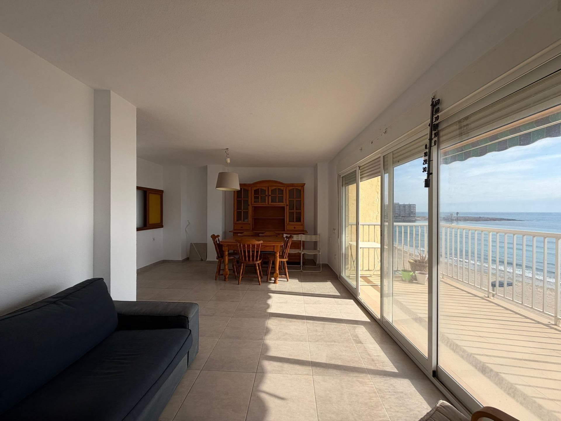 On the shores of the Mediterranean, in one of the most privileged enclaves of Torrevieja, stands an apartment that redefines the meaning of living in front of the sea. This home, with its four large bedrooms and two bathrooms, is presented as a haven of serenity where the sound of the waves sets the rhythm of each day. From the first moment, the home transmits a feeling of absolute calm, that unique sensation that is only found when the sea becomes part of your daily life. First impressions are unforgettable. As soon as you enter, natural light takes over the space, reflecting on well-kept surfaces and giving life to each room. The spaciousness of the apartment is perceived from the hall: each room seems designed to make the most of the clarity and the landscape, achieving an enveloping, bright and warm atmosphere. There is no corner that does not evoke well-being, nor moment that does not invite rest. The main living room, which acts as the heart of the home, opens towards the blue horizon, visually connecting the interior with the exterior in an almost imperceptible transition. The chosen furniture combines comfort and style, creating a cozy atmosphere where everything fits together effortlessly. The veins of the floor, the texture of the fabrics, the soft tones of the walls... everything comes together in a single intention: to live without haste, surrounded by beauty, with the sea as a constant witness. The kitchen, fully equipped and designed for everyday use, integrates naturally into the whole, maintaining the same philosophy of comfort and functionality. Here everything is ready for those who enjoy sharing moments with family or friends. Cooking with the sea breeze gently entering through the window or having breakfast while the golden morning light bathes the room is a privilege that transforms each routine into a pleasant experience. The four rooms provide spaciousness and versatility, allowing them to easily adapt to different lifestyles. Whether it is a family looking for space and privacy, a couple who wants to maintain an office or reading room, or even those who plan to receive visitors, this apartment offers endless possibilities. In all of them, the decoration follows the same criteria: neutral tones, noble materials and a continuous feeling of openness to the outside predominate. Sleeping listening to the sea, waking up to the light that filters through light curtains, opening the windows and breathing in the salty breeze: these are simple gestures that become small daily luxuries. The two bathrooms, spacious and comfortable, reflect the same spirit of balance and well-being. Everything is arranged to offer comfort and freshness, in a cozy environment that invites you to relax. The spaces, well distributed and functional, maintain a coherent aesthetic with the rest of the apartment, combining elegance and practicality. The real charm, however, is revealed when crossing onto the terrace. There the Mediterranean appears in all its splendor: a changing landscape that accompanies every season and every moment of the day. In the morning, the sun's reflections turn the water into golden tones; At sunset, the colors become warm and enveloping, offering a natural spectacle that is never repeated in the same way. This outdoor space, perfect for resting, reading, having breakfast or simply contemplating the horizon, becomes the soul of the home. Living here means living with the sea, with its constant presence, with its sound that accompanies both silence and conversation. The location, on the first line, makes this apartment a jewel of Torrevieja. From this privileged position you can easily access the promenade, the best-known beaches and a wide range of restaurants, cafes and shops.