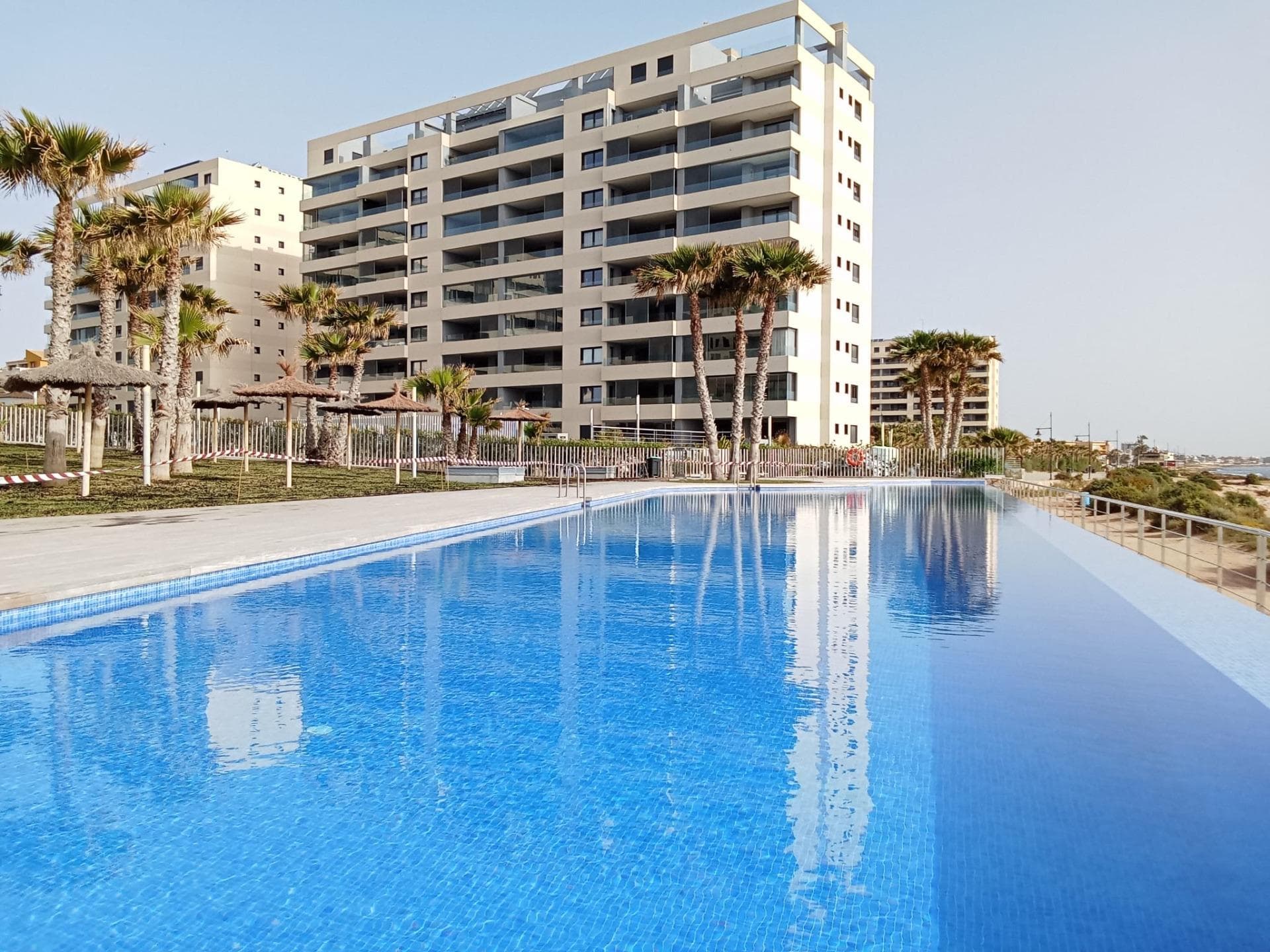 Ground floor apartment with elegant and modern design, like-new apartment, a few steps from the sea in Punta Prima! It consists of a living room with an open kitchen with access to the large covered terrace (approximately 16 m2) and the garden (approximately 65 m2), two double bedrooms with built-in wardrobes, two bathrooms and an underground parking space with a storage room in the same building. The main bedroom has an en suite bathroom and access to the terrace. Furnished. Equipped kitchen. Ducted air conditioning and heating. Bathrooms with underfloor heating. Video intercom. South facing. Top-quality materials. Direct elevators access from the apartment to the parking and storage units. Concierge and video surveillance. Residential with 3 swimming pools (Infinity, heated and children’s pools) with sea views, outdoor jacuzzi, children’s play areas and gardens. Close to all amenities, cafes, supermarkets, … A luxury! With a privileged location, a few steps from the sea, perfect to enjoy the beach and the great Mediterranean climate