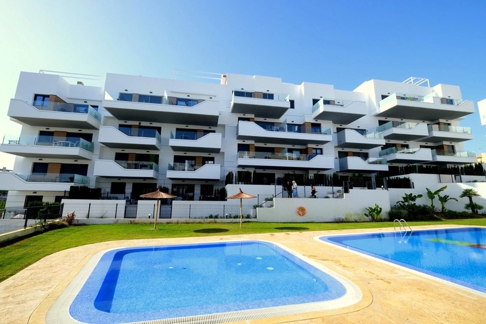 Stunning modern Apartment in Villamartín area, 2 bed 1 bath, terrace with pool views, underground parking – Ready to move in !Positioned within one of Villamartín’s most desirable residential communities, this exceptional first-floor apartment, completed in 2023, embodies modern elegance, comfort, and refined Mediterranean living.From the moment you enter through the reinforced security door, you are welcomed into a beautifully curated interior where clean architectural lines meet premium finishes and bespoke designer furnishings. The open-concept living space is both bright and inviting, seamlessly integrating a fully fitted American-style kitchen with a stylish dining and lounge area—perfectly designed for both relaxation and entertaining.Floor-to-ceiling sliding doors open onto a private east-facing terrace, bathed in gentle morning and midday sunlight. From here, enjoy tranquil open views across the impeccably landscaped gardens and the elegant communal pool, creating a serene and exclusive atmosphere.The apartment offers two generously proportioned bedrooms, each featuring built-in wardrobes and a calming, contemporary aesthetic. The master suite enjoys direct access to a beautifully appointed bathroom with a walk-in shower, thoughtfully designed with dual access from both the bedroom and the living area—combining luxury with practicality.Every detail of this residence reflects quality and comfort. The property is offered fully furnished with high-end designer pieces, allowing for an effortless, turnkey experience. Integrated ducted air conditioning (hot and cold) ensures year-round climate control, while the building provides lift access throughout, including to the secure underground garage with a private parking space.Set within an exclusive gated community, residents benefit from exceptional amenities including lush landscaped gardens, a stunning swimming pool for adults and children, a heated jacuzzi, and pétanque courts—all designed to enhance a relaxed yet sophisticated lifestyle.Despite its peaceful and private setting, the apartment is ideally located just a short stroll from the vibrant Villamartín Plaza and La Fuente Commercial Centre, offering a fine selection of restaurants, cafés, and amenities. World-class golf courses—Villamartín, Campoamor, Las Ramblas, and Las Colinas—are only minutes away, while the pristine blue flag beaches of Orihuela Costa and the renowned Zenia Boulevard shopping destination are within a 10-minute drive. Both Alicante and Corvera airports are conveniently accessible in approximately 45 minutes.A truly exceptional property offering style, comfort, and prime location—perfect as a distinguished holiday retreat, investment, or permanent residence. Early viewing is highly recommended.