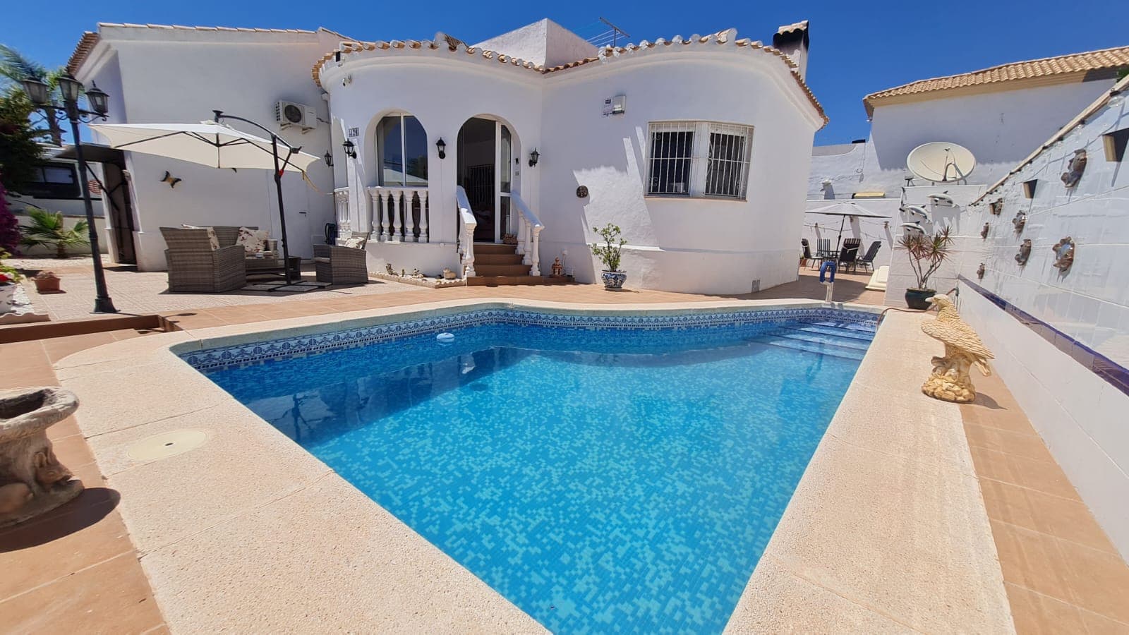 Nestled within the highly desirable residential area of La Florida, Orihuela Costa, this beautifully maintained detached villa offers the perfect combination of traditional Mediterranean charm, privacy, and comfortable single-level living. Set on a generous 238m² plot and enjoying a sought-after south-west orientation, this inviting home is ideal for those seeking a permanent residence, holiday retreat, or investment property in one of the Costa Blanca's most established and convenient locations.From the moment you arrive, the villa exudes warmth and character. A bright glazed conservatory welcomes you into the property, providing a wonderful additional living space that can be enjoyed throughout the year. Whether used as a morning sitting area, reading room, or dining space, it creates a seamless transition between the indoor and outdoor areas.Inside, the property offers a spacious and welcoming lounge centred around a charming wood-burning fireplace, creating a cosy atmosphere during the cooler months. The open-plan kitchen and dining area flow naturally from the living space, making the home both practical and sociable for everyday living and entertaining.The accommodation comprises two generous double bedrooms with fitted wardrobes and two bathrooms, providing comfort and convenience for both owners and guests. An additional multi-purpose room is currently used as a home office but could easily serve as a hobby room, dressing room, storage area, or occasional guest accommodation depending on individual requirements.The true heart of this home lies outdoors. Designed to embrace the relaxed Mediterranean lifestyle, the villa features a beautiful private saltwater swimming pool surrounded by attractive terraces and a variety of charming seating areas. These private outdoor spaces create the perfect environment for sunbathing, outdoor dining, entertaining friends and family, or simply unwinding in the sunshine. The property's south-west orientation ensures excellent afternoon and evening sun, allowing owners to make the most of outdoor living throughout the year.A further highlight is the impressive 38m² private rooftop solarium. From here, you can enjoy pleasant open views across the surrounding area and nearby green spaces while benefiting from all-day sunshine. The solarium also offers exciting potential for future expansion, with several neighbouring properties having successfully incorporated additional living accommodation, subject to the relevant permissions.The villa is offered fully furnished and benefits from air conditioning, a private garage, low-maintenance gardens, and the significant advantage of having no community fees, helping to keep ongoing ownership costs low.La Florida remains one of Orihuela Costa's most popular residential areas thanks to its excellent range of amenities and convenient location. A wide selection of restaurants, cafés, bars, supermarkets, and everyday services can be reached on foot, while the popular Playa Flamenca market and the renowned La Zenia Boulevard shopping centre are both just a few minutes away. The beautiful sandy beaches of Playa Flamenca, La Zenia, Cabo Roig, and Campoamor are all within easy reach, offering some of the finest coastline on the Costa Blanca.Golf enthusiasts will appreciate being close to several championship courses, including Villamartín Golf, Las Ramblas Golf, Real Club de Golf Campoamor, and the prestigious Las Colinas Golf & Country Club.Combining character, privacy, generous outdoor space, and a superb location close to every amenity, this charming villa offers an exceptional opportunity to enjoy the very best of Costa Blanca living. Properties with private pools, no community fees, and this level of outdoor space in La Florida are becoming increasingly difficult to find, making early viewing highly recommended.