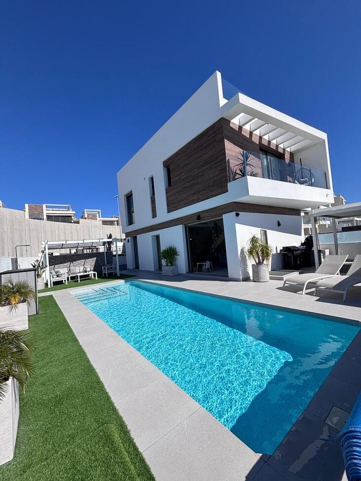 Beautiful 5-Bedroom Contemporary Villa with Heated Pool This stunning southwest-facing corner plot villa offers modern luxury, generous space, and beautiful views, making it the perfect home for both permanent living or holidays in the sun.The property features 5 spacious bedrooms, 3 bathrooms and a guest WC, split between 3 levels, all designed with comfort and practicality in mind. The main bedroom boasts a stylish ensuite bathroom and walk-in wardrobe, while the additional bedrooms include built-in wardrobes, providing excellent storage throughout.At the heart of the home is a large open-plan kitchen and living area, creating a bright and sociable space ideal for family living and entertaining. The villa benefits from hot and cold air conditioning, ensuring year-round comfort.Outside, the beautifully designed garden offers everything you need to enjoy the Mediterranean lifestyle. The private heated swimming pool is surrounded by sunbathing areas as well as comfortable shaded seating spaces, perfect for relaxing or hosting guests. There is also a children’s play area, making it ideal for families.The villa sits on a desirable corner plot with southwest orientation, allowing you to enjoy sunshine throughout the day and spectacular views from both the garden and balcony.Additional features include private parking for two cars, a practical utility area, and a spacious underbuild which provides two additional bedrooms, a bathroom with shower, offering flexible accommodation for guests or extended family.The property is sold fully furnished and has been finished with high-quality silicone exterior paint, providing durability and a fresh modern appearance.A truly exceptional home combining space, style, and breathtaking views