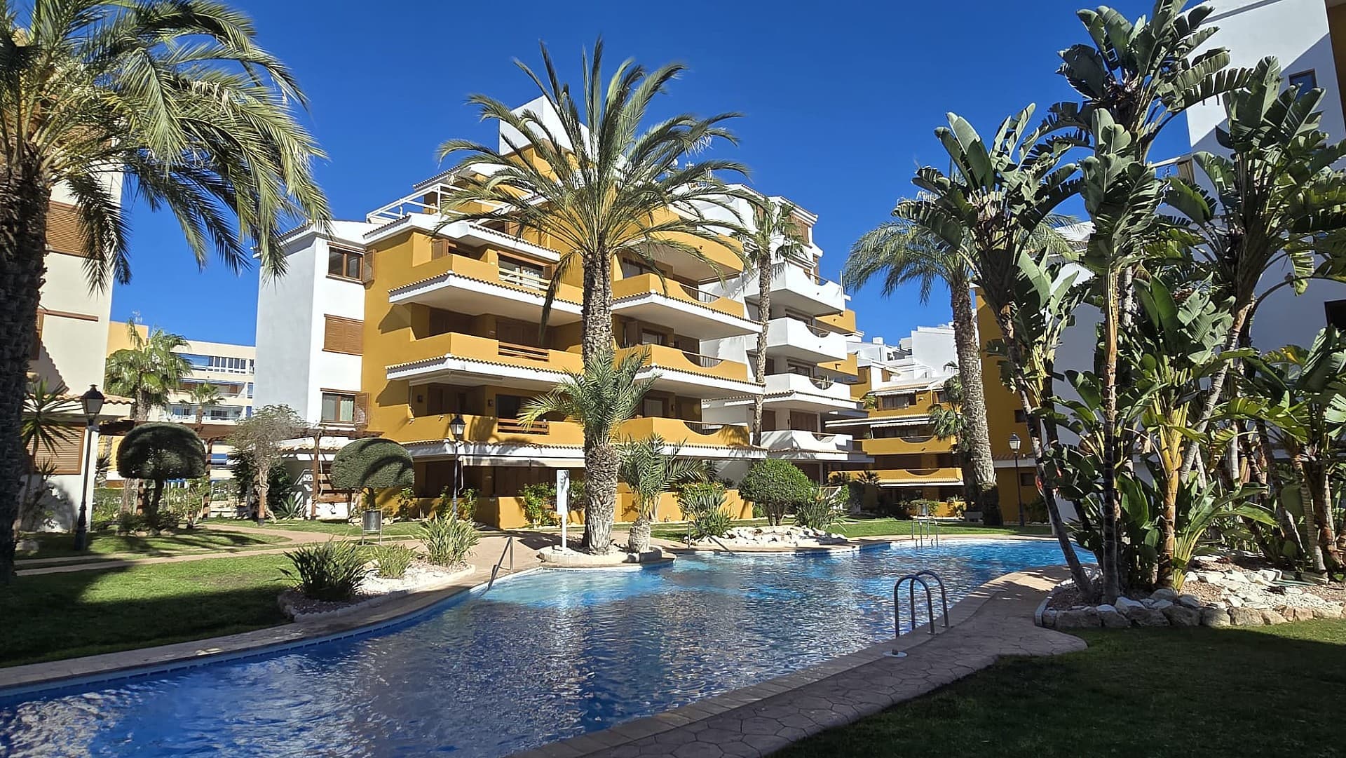. Sunny Corner Apartment with Pool View in Punta PrimaThis luxury corner apartment in Residencial La Entrada (Punta Prima) offers a sunny terrace overlooking the swimming pool and the communal gardens. The apartment features 2 bedrooms, 2 bathrooms (one en-suite with a walk-in shower), an open-plan kitchen, and a spacious living room with direct access to the terrace. Thanks to its south-facing orientation, you can enjoy the sun all year round.The apartment is located on the first floor (accessible by elevator) and includes a private parking space in the underground garage. Just 500 meters from the beaches, restaurants, and supermarkets, this is the perfect location for both permanent living and a holiday home.This apartment also comes fully furnished!