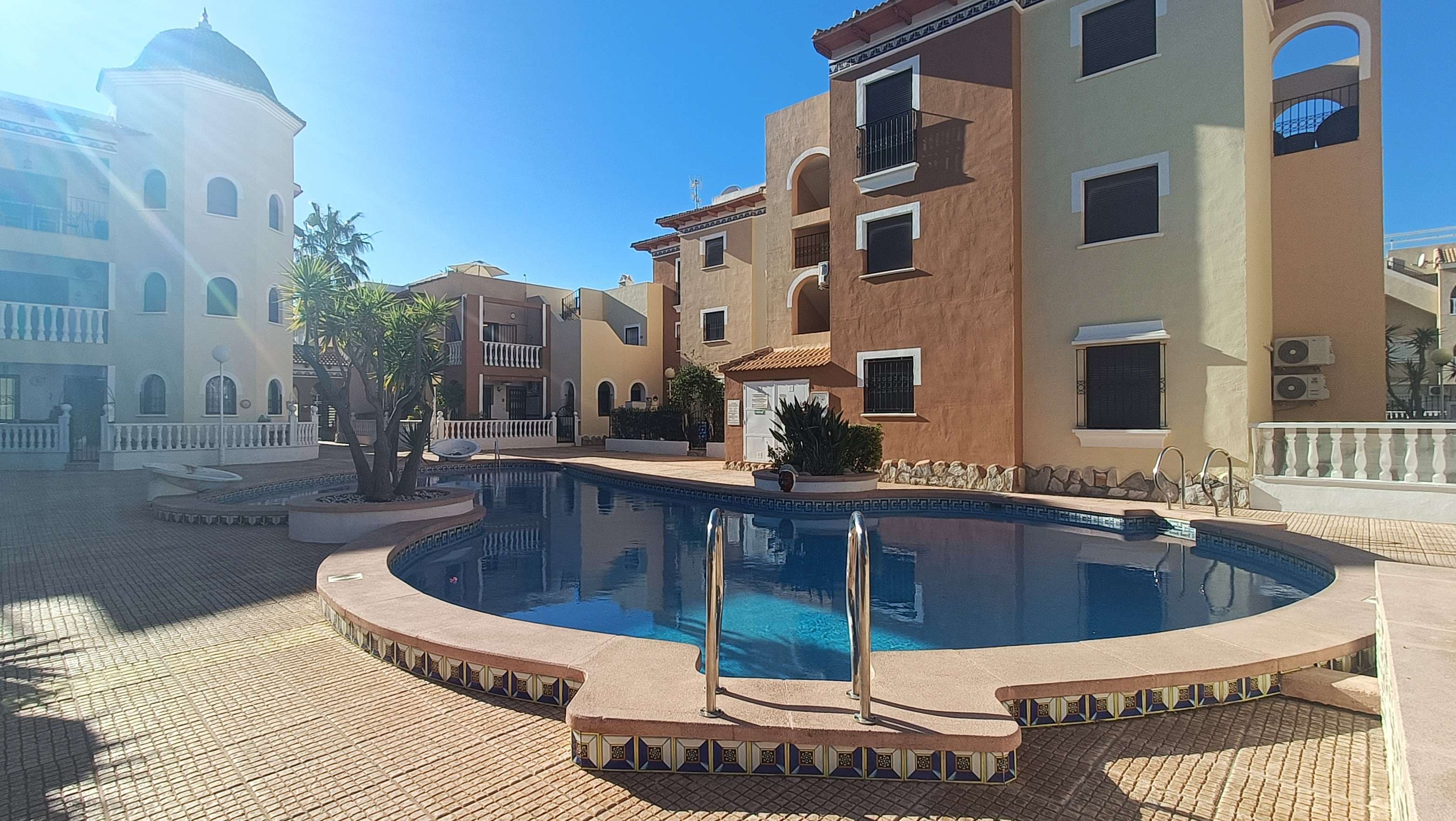 Beautifully presented first-floor apartment with private solarium located in the charming coastal town of Los Alcázares, set within a highly sought-after gated community known for its award-winning communal gardens and stunning swimming pool.Accessed via a staircase, the apartment welcomes you into a bright and stylish open-plan living space, combining a comfortable lounge, fully fitted kitchen and dining area. The space has been tastefully decorated throughout, creating a warm and inviting atmosphere that is ready to move straight into. From the living area, you can step out onto a charming balcony overlooking the beautiful communal pool – the perfect spot to enjoy a morning coffee while taking in the peaceful surroundings.A hallway leads to a well-proportioned guest bedroom with a double bed and built-in wardrobes, a spacious family bathroom, and the bright master bedroom featuring built-in wardrobes, a private en-suite bathroom and double sliding doors opening onto a Juliet balcony, allowing plenty of natural light to fill the room.An external staircase leads up to the apartment’s standout feature – a very large private rooftop solarium. Offering 360-degree views and enjoying sunshine from sunrise to sunset, this fantastic space provides ample room for sunbathing, outdoor dining, entertaining friends and family, or simply relaxing while making the most of the Mediterranean climate.The apartment is being sold partly furnished, with the current owners only taking a few personal items, making it a fantastic ready-to-move-in opportunity. Perfectly positioned within the community, the property enjoys one of the best views in the complex while still maintaining a great sense of privacy. Additional features include air conditioning and access to the beautifully maintained communal pool and landscaped gardens that have won awards for their design and upkeep. The community itself is friendly and well established.Ideally located, the property is just a 2-minute drive from Playa Lo Sola and within walking distance of a wide range of amenities including shops, bars, restaurants and the beach. This makes the apartment perfect as a permanent residence, holiday home or investment property.Los Alcázares is a popular coastal town on the shores of the Mar Menor, well known for its beautiful sandy beaches, relaxed atmosphere and year-round sunshine. The town offers a fantastic selection of restaurants, bars, shops and leisure facilities, as well as a lovely promenade ideal for walking or cycling along the waterfront. With several golf courses nearby and easy access to Murcia International Airport, Los Alcázares has become a favourite destination for both holidaymakers and those looking to enjoy the Mediterranean lifestyle all year round.Call us today to arrange your viewing and take the first step towards finding your dream home. Our experienced agents specialise in this area and will be delighted to help you find the perfect property to match your lifestyle.
